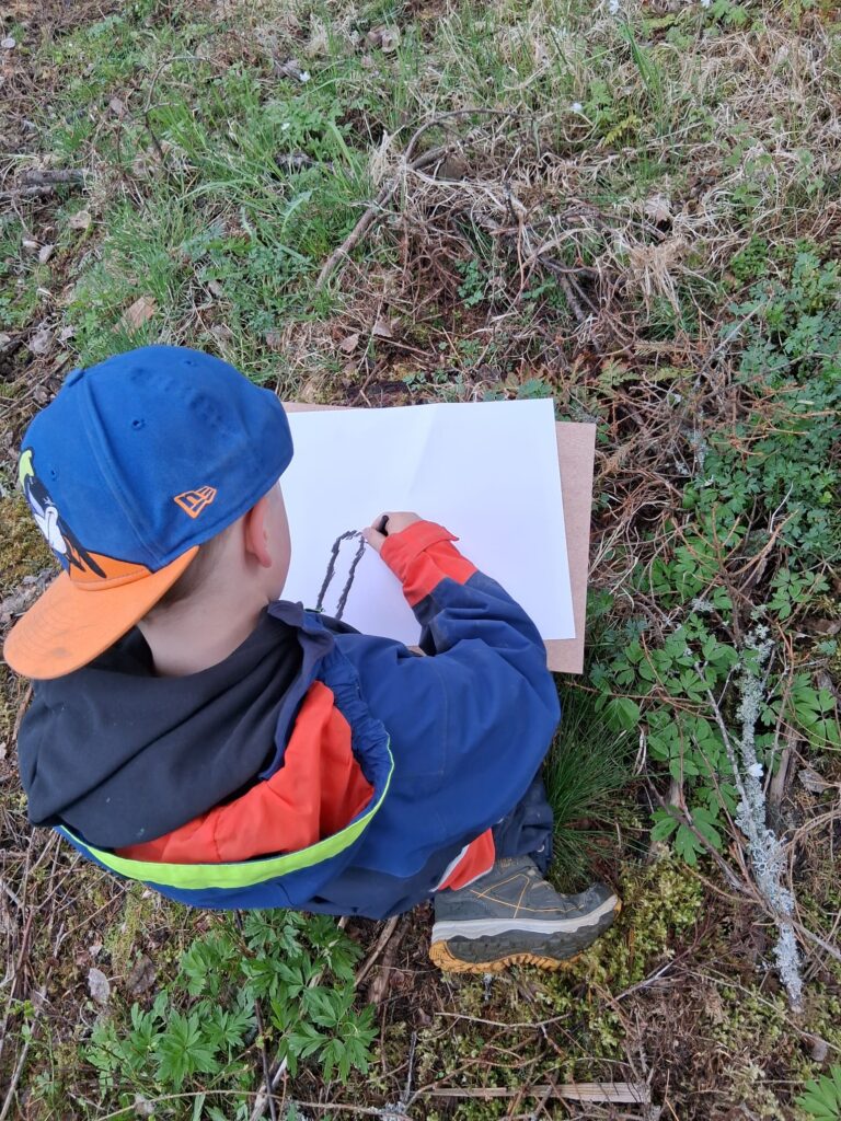 Lapsi piirtää hiilellä paperille metsässä.